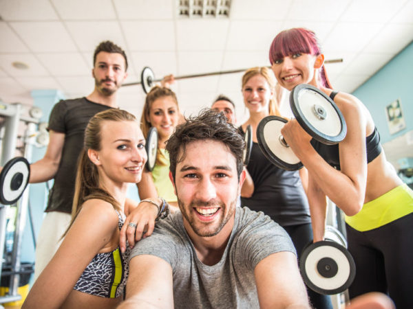 Group of sportive people in a gym taking selfie - Happy sporty friends in a weight room while training - Concepts about lifestyle and sport in a fitness club